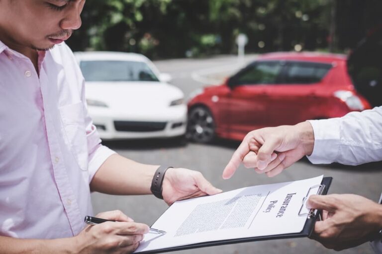 Insurance agent assessing damaged car while customer completes accident claim form.