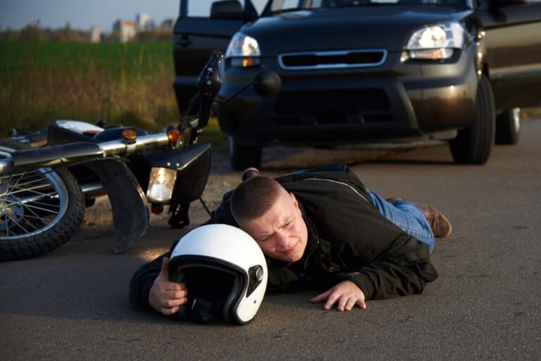 After the dangerous collision, a injured motorcyclist lies on the road near car and motorcycle in Madison, WI