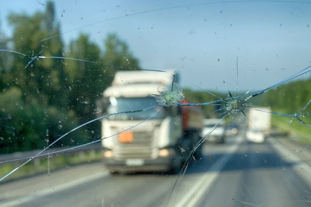View of a highway seen through a shattered windshield, the aftermath of an encounter with a truck carrying crushed stone.