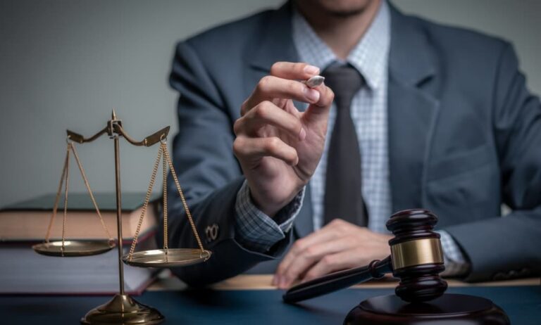 lawyer sits at his desk wearing a gray suit, there is a scale representing justice on the desk