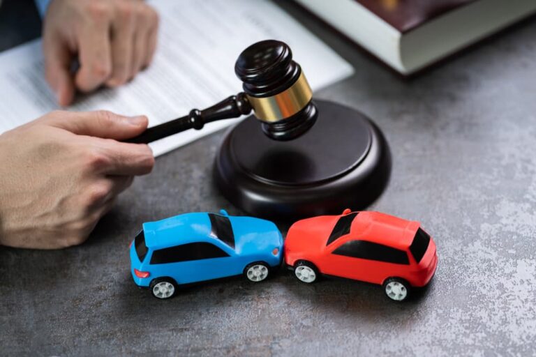 a judge's gavel strikes atop a table next to a pair of model cars mimicking a Sue After Car Accident car accident