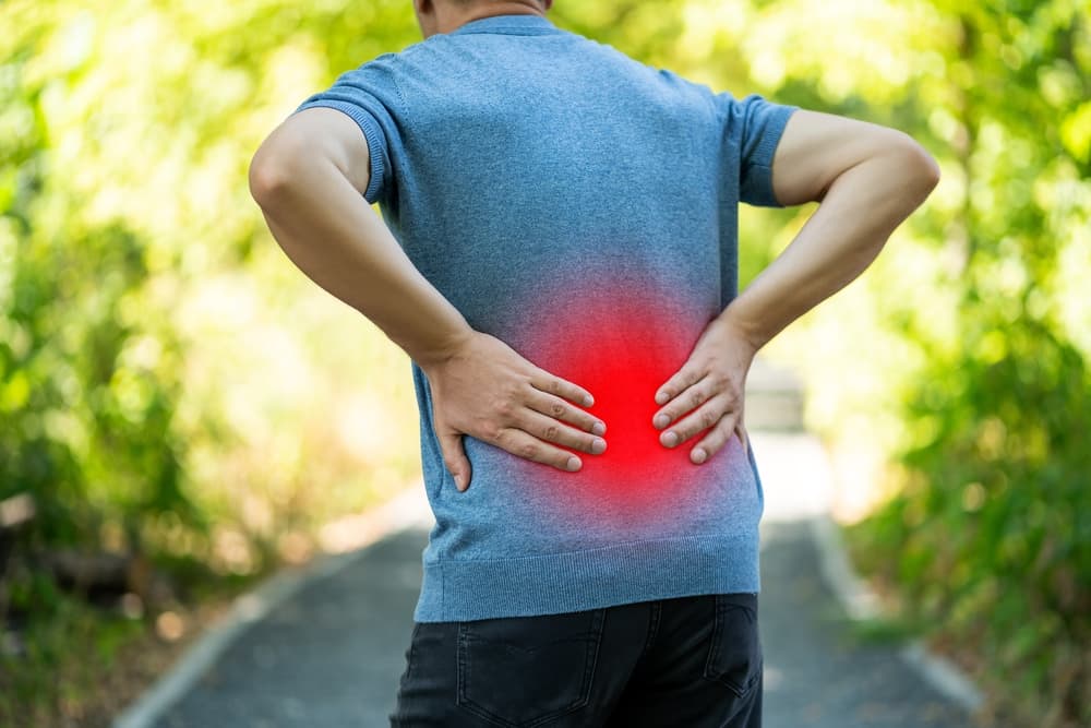 Man experiencing back pain while walking outdoors, representing kidney inflammation and health issues.