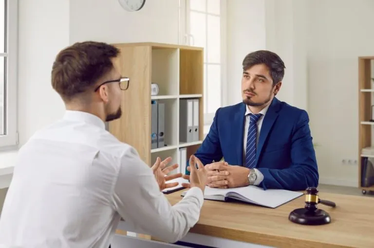 Young man discusses his problem with a serious lawyer in a formal suit at the office desk, emphasizing attentive listening.