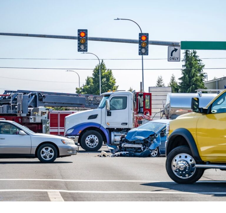 Car crash at traffic light with damaged vehicles, fire truck, and onlookers on the scene.