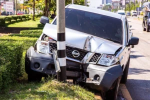 A car collision has occurred, impacting a street light pole within the residential community. The front of the vehicle has sustained significant damage.