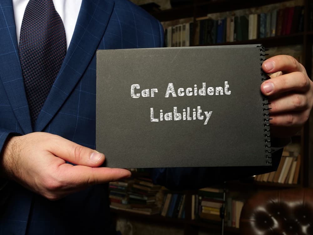 Create a conceptual photograph illustrating the concept of car accident liability, accompanied by a handwritten phrase.