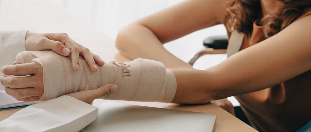 An orthopedic doctor closely examines a woman patient's broken arm, carefully applying a splint and plaster cast. Such injuries often occur from falls and accidents, causing trauma to the affected area. 