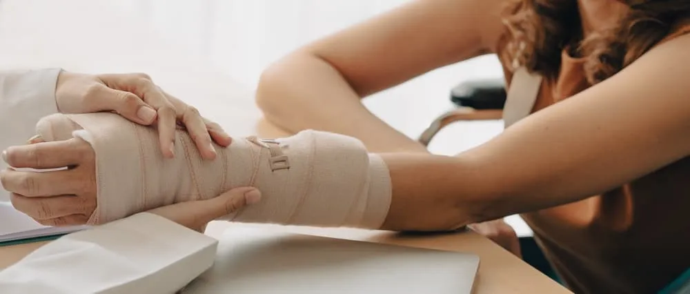 An orthopedic doctor closely examines a woman patient's broken arm, carefully applying a splint and plaster cast. Such injuries often occur from falls and accidents, causing trauma to the affected area.