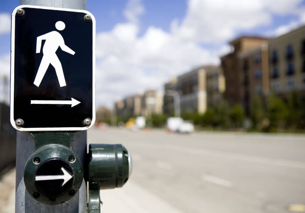 a medium-distance view of a crosswalk sign on a traffic post with an arrow directing the pedestrian to travel across the road