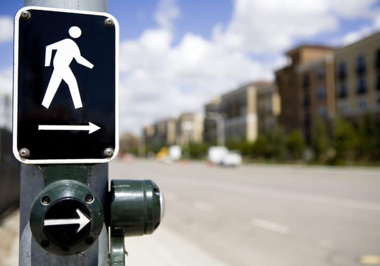 a medium-distance view of a crosswalk sign on a traffic post with an arrow directing the pedestrian to travel across the road