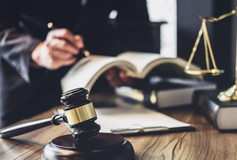 a lawyer makes notes in a ledger next to a gavel and scales atop a desk