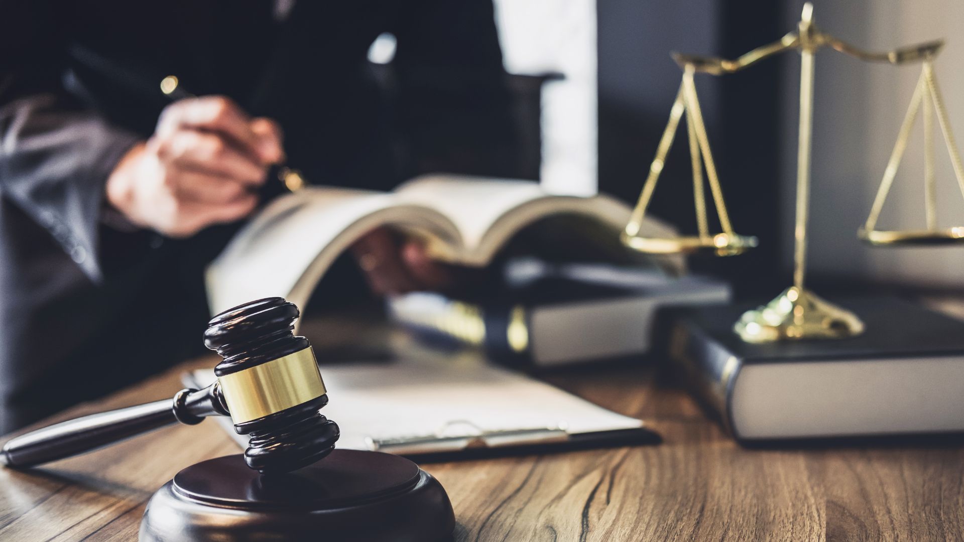 a lawyer makes notes in a ledger next to a gavel and scales atop a desk