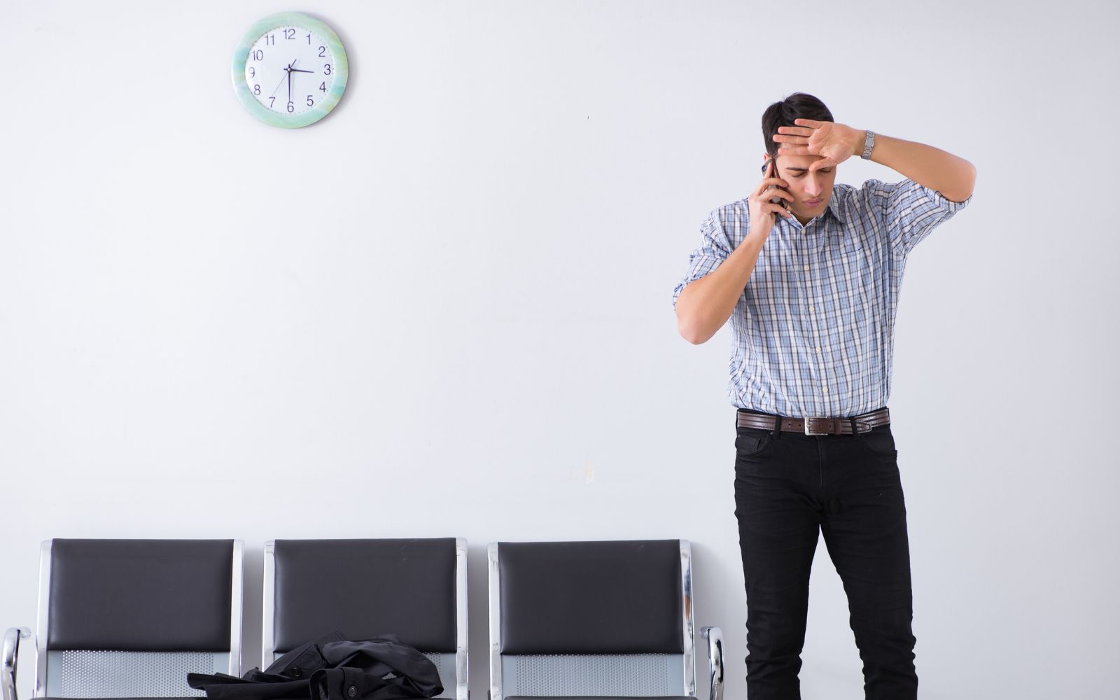 a man in a gray button down shirt uses a cell phone in a waiting room, he appears to be confused or frustrated