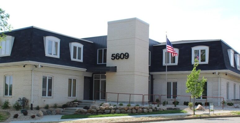 a beige and brown office building with an American flag and greenery out front