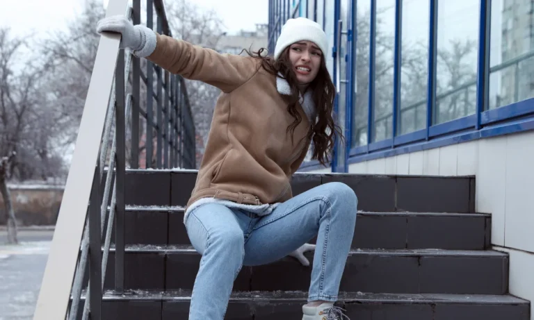A woman in a brown coat slips and falls on slippery steps