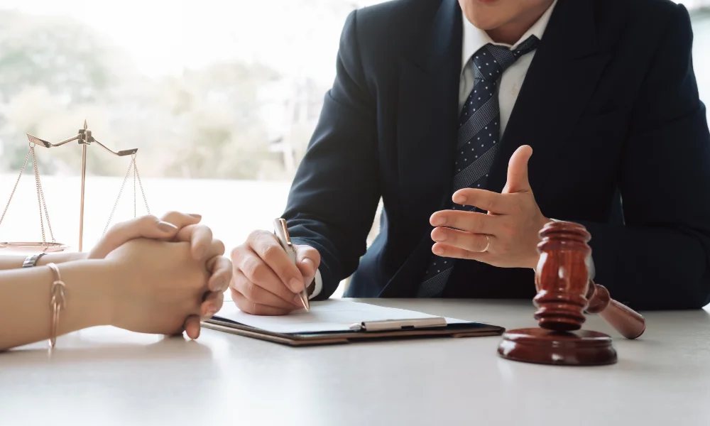 an injury lawyer meets with a client, their hands are folded atop a desk next to a set of justice scales