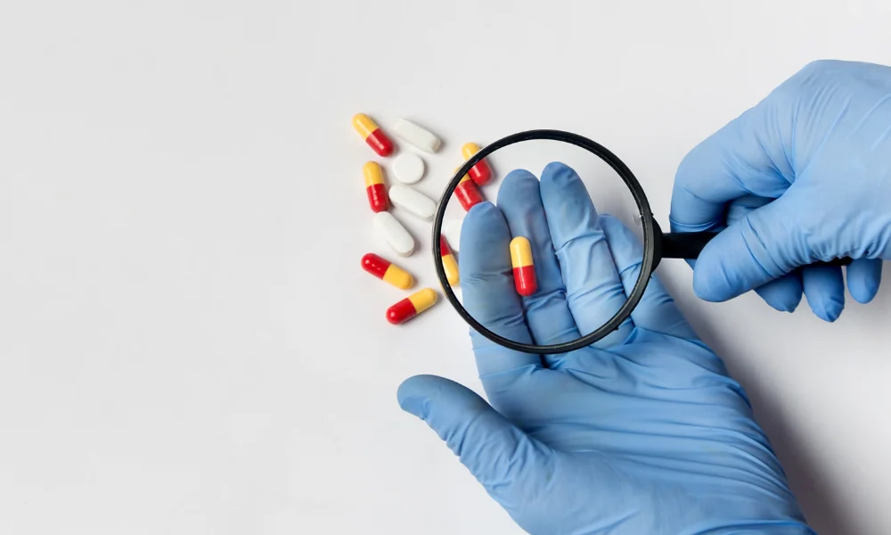 a person in sterile gloves inspects a pill product with their magnifying glass