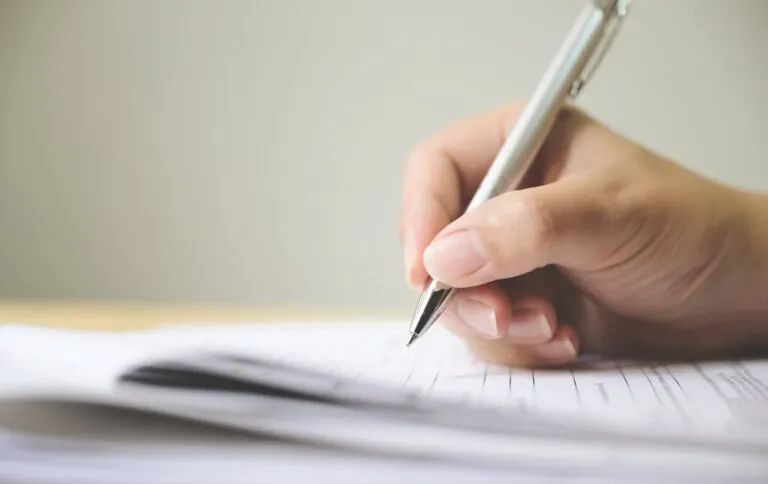 Man's hand signing a document application form.